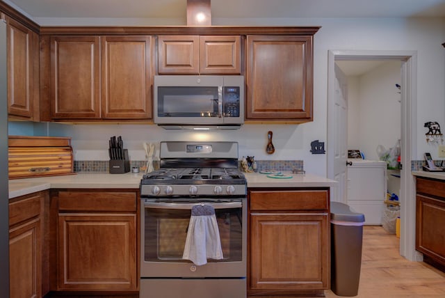kitchen featuring light countertops, light wood-style flooring, appliances with stainless steel finishes, and washer / clothes dryer