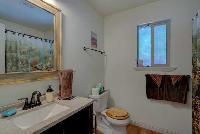 bathroom with wood finished floors, vanity, baseboards, toilet, and visible vents