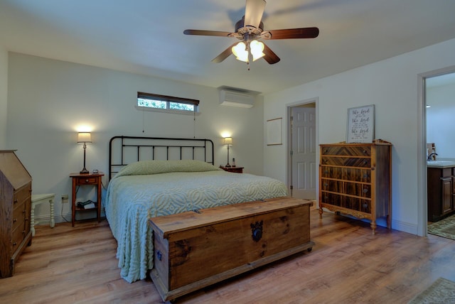 bedroom with connected bathroom, a sink, a wall mounted AC, light wood-style flooring, and ceiling fan
