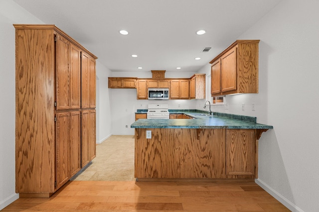 kitchen with a sink, brown cabinetry, stainless steel microwave, a peninsula, and white range oven