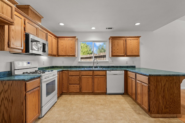 kitchen featuring dark countertops, a sink, white appliances, a peninsula, and visible vents