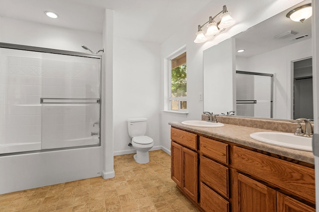 bathroom with double vanity, combined bath / shower with glass door, toilet, and a sink