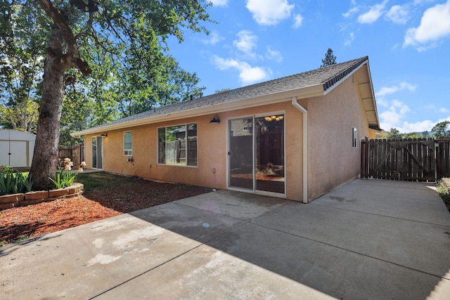 back of house with a patio area, an outbuilding, a shed, and stucco siding