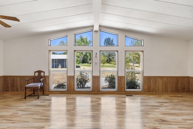 interior space with a wainscoted wall, vaulted ceiling with beams, a ceiling fan, wood walls, and wood finished floors