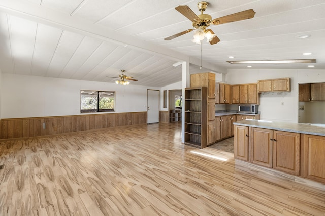 kitchen with wainscoting, lofted ceiling with beams, ceiling fan, light wood-style flooring, and stainless steel microwave