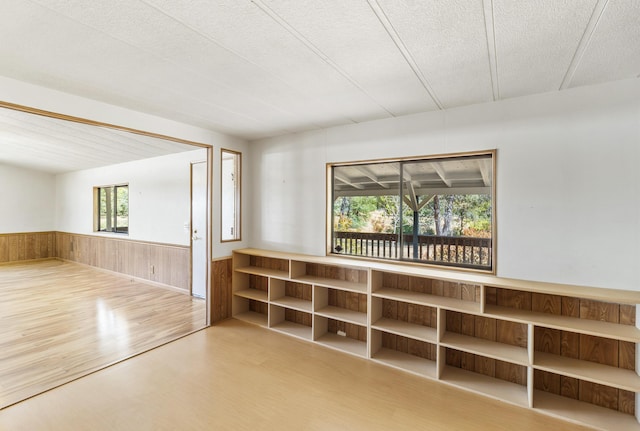 empty room with wainscoting, wood walls, wood finished floors, and a textured ceiling