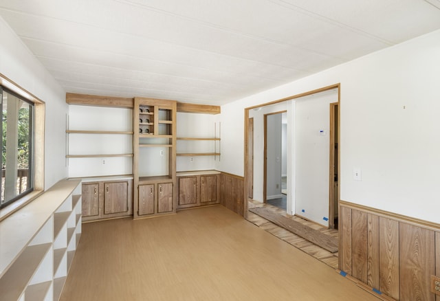empty room featuring wainscoting, wooden walls, and light wood-style flooring