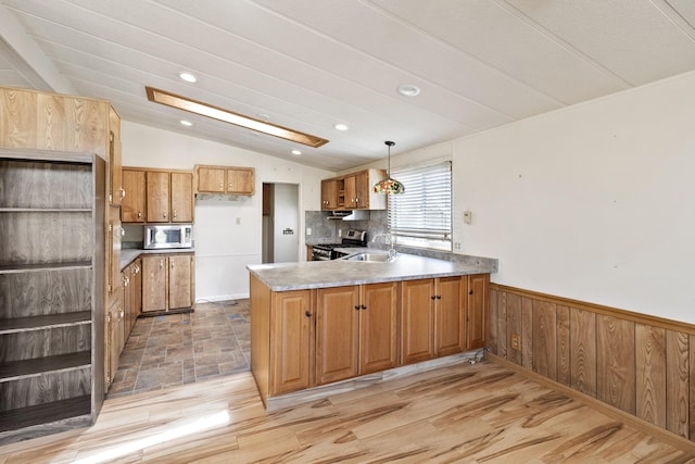 kitchen with vaulted ceiling, a sink, a peninsula, brown cabinetry, and appliances with stainless steel finishes
