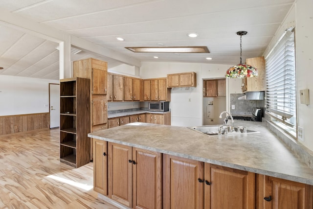 kitchen with a peninsula, a sink, stainless steel microwave, wainscoting, and vaulted ceiling with beams