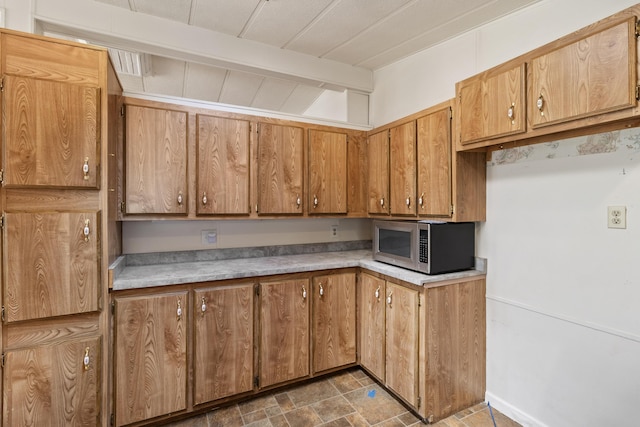 kitchen with brown cabinetry, stainless steel microwave, beam ceiling, and light countertops