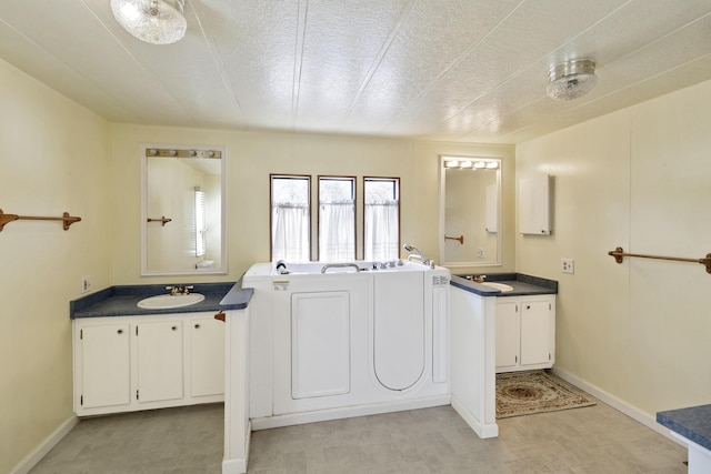 laundry area with a sink, baseboards, separate washer and dryer, cabinet space, and a textured ceiling