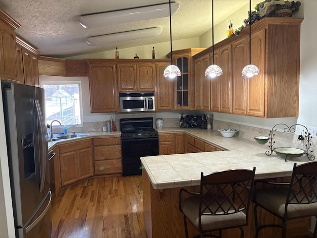 37150 Sapphire Rd, Burney, CA 96013 - kitchen featuring appliances with stainless steel finishes, a peninsula, vaulted ceiling, light wood-style floors, and glass insert cabinets