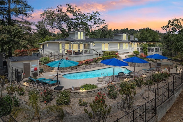 back of property at dusk with a storage shed, a fenced in pool, an outbuilding, fence, and a patio