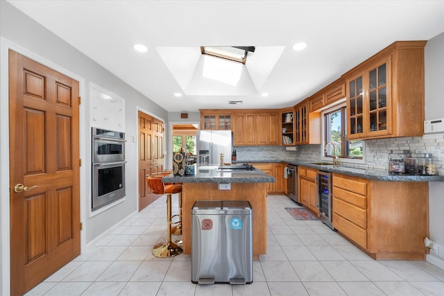 kitchen featuring wine cooler, a sink, a healthy amount of sunlight, brown cabinetry, and appliances with stainless steel finishes