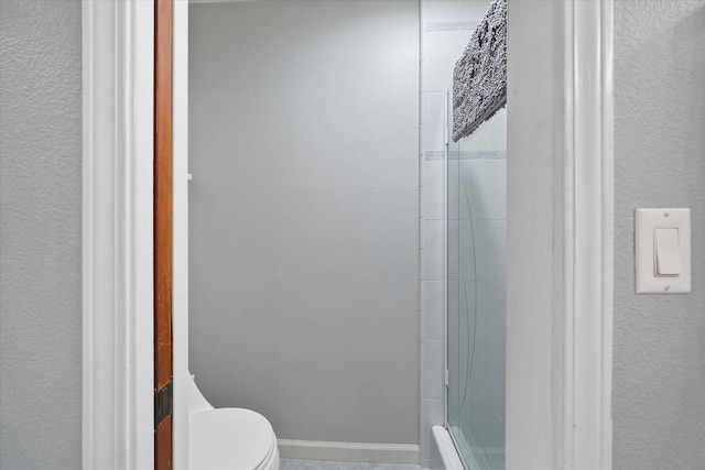 bathroom featuring baseboards, a shower with door, and toilet