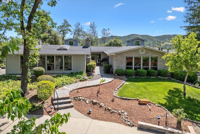 view of front of house featuring a chimney, a mountain view, stone siding, and a front yard