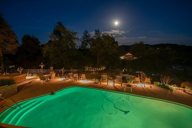 pool at night with a community pool, a patio area, and fence