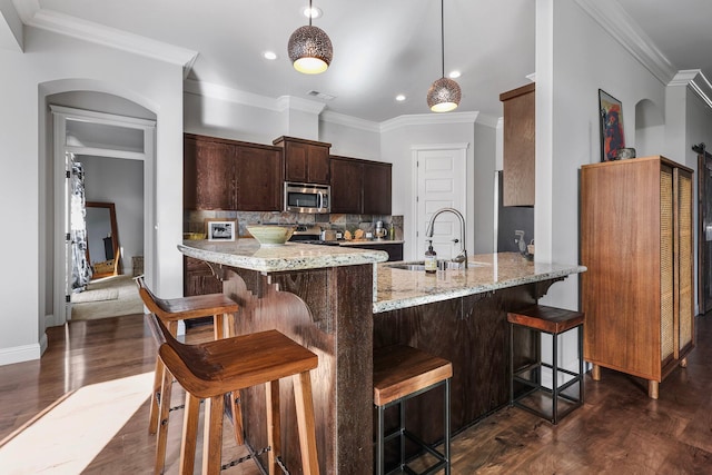 kitchen with dark wood-style flooring, appliances with stainless steel finishes, light stone counters, a sink, and backsplash