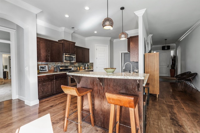 kitchen with arched walkways, a breakfast bar area, stainless steel appliances, and dark brown cabinetry