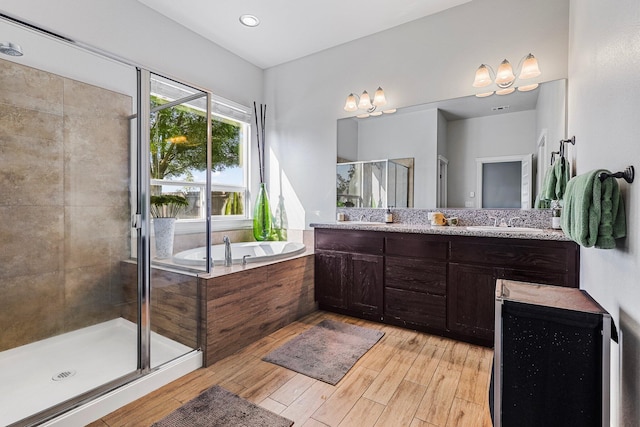full bathroom with double vanity, a garden tub, a stall shower, a sink, and hardwood / wood-style floors
