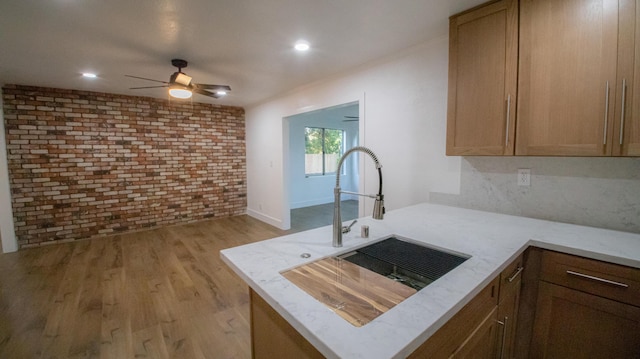 kitchen featuring a sink, light wood-type flooring, brick wall, ceiling fan, and a peninsula