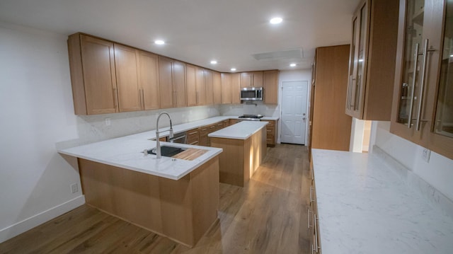 kitchen featuring stainless steel microwave, light wood-type flooring, a center island, and a sink