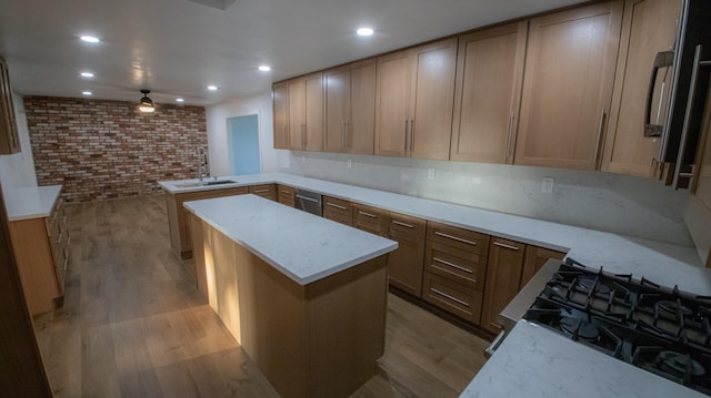 kitchen featuring light wood finished floors, a sink, a kitchen island, a peninsula, and brick wall