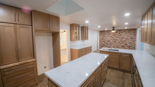 kitchen with light wood-type flooring, a center island, a sink, and light stone countertops