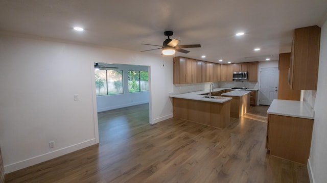 kitchen with stainless steel microwave, a peninsula, wood finished floors, and a sink