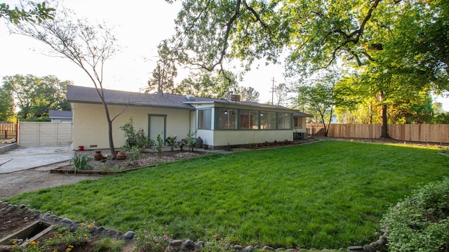 back of house with a lawn, a sunroom, a fenced backyard, and stucco siding