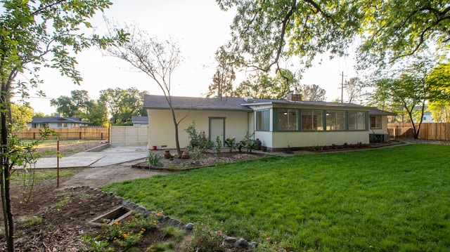 rear view of property featuring a lawn, driveway, fence, stucco siding, and a sunroom