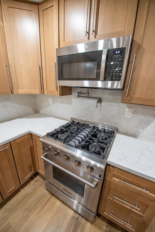 kitchen with light wood finished floors, light stone counters, and appliances with stainless steel finishes