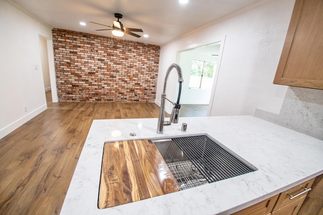 kitchen featuring a sink, brick wall, wood finished floors, ceiling fan, and crown molding