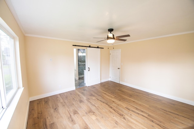 spare room featuring a barn door, ornamental molding, light wood finished floors, and ceiling fan