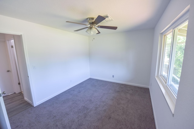 carpeted spare room with baseboards, visible vents, a ceiling fan, and a wealth of natural light