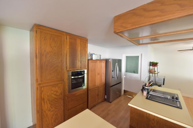 kitchen with light wood-type flooring, light countertops, appliances with stainless steel finishes, and brown cabinets