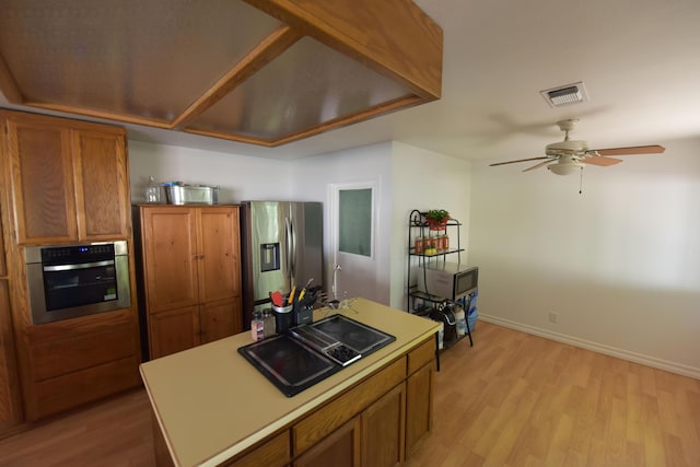 kitchen featuring brown cabinets, light wood-style flooring, stainless steel appliances, a ceiling fan, and visible vents