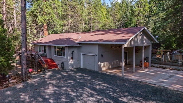 view of front of home with a shingled roof, a forest view, driveway, an attached garage, and fence