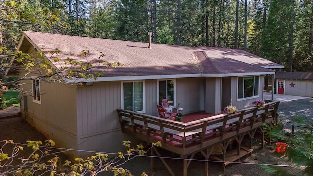 back of house featuring an outbuilding, a deck, and a shingled roof