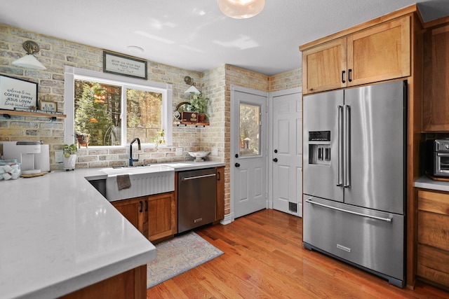 kitchen with brown cabinets, a sink, light wood-style floors, light countertops, and appliances with stainless steel finishes