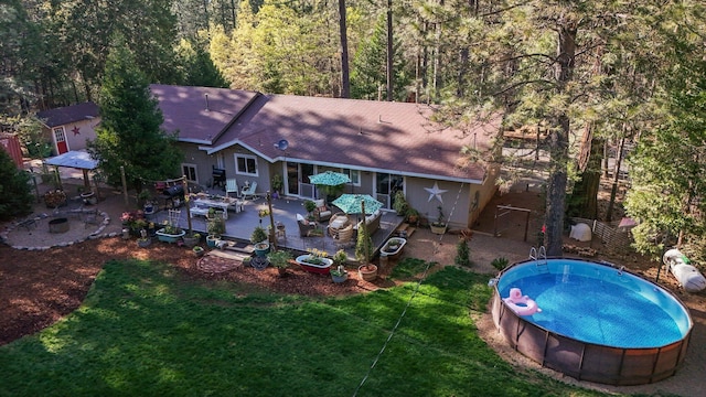 exterior space featuring roof with shingles, a yard, a forest view, and a patio area