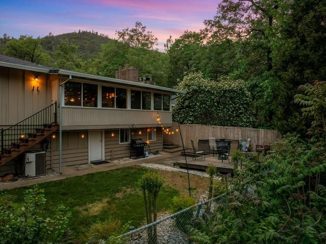 19817 Oak Knoll Dr, Lakehead, CA 96051 - back of house at dusk with a sunroom, stairs, a wooden deck, and fence