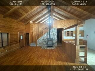 unfurnished living room featuring wooden ceiling, wood finished floors, beam ceiling, a wood stove, and high vaulted ceiling