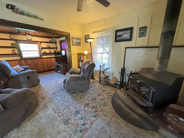 living area with wood walls, ceiling fan, a wood stove, and wooden ceiling