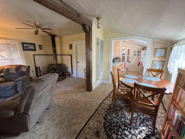 dining room featuring light colored carpet, a ceiling fan, a wood stove, and wooden ceiling