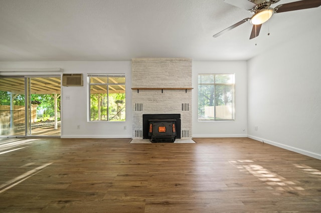 unfurnished living room with wood finished floors, baseboards, ceiling fan, a wood stove, and an AC wall unit