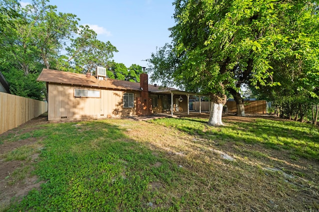back of house featuring a chimney, a lawn, and a fenced backyard