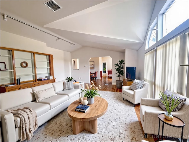 living area featuring rail lighting, visible vents, vaulted ceiling, arched walkways, and wood finished floors