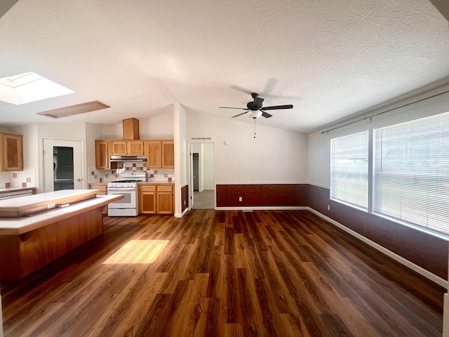 kitchen with vaulted ceiling with skylight, light countertops, white range with gas cooktop, dark wood-style floors, and under cabinet range hood