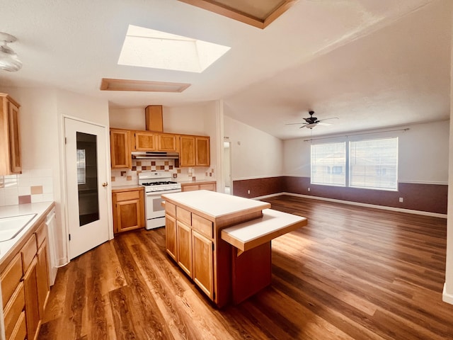 kitchen featuring white appliances, under cabinet range hood, light countertops, dark wood-style flooring, and a sink